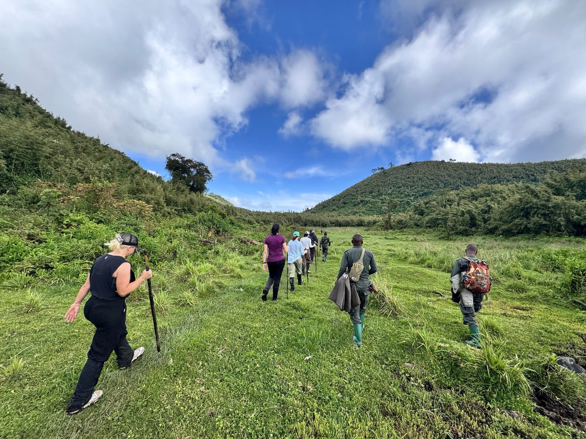 Hikers walking up a green valley below the Virunga volcanoes