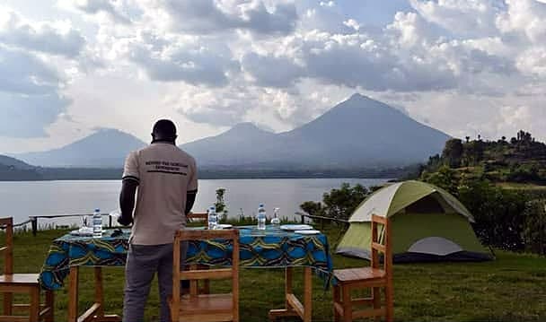 Guide by a lunch table and tent, with the volcanoes across the lake